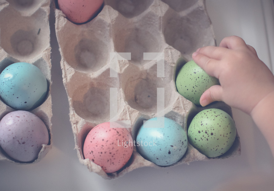 a toddler touching dyed speckled Easter eggs 