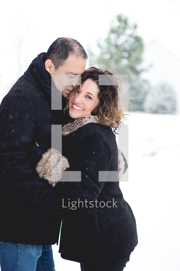 a married couple hugging in the snow 