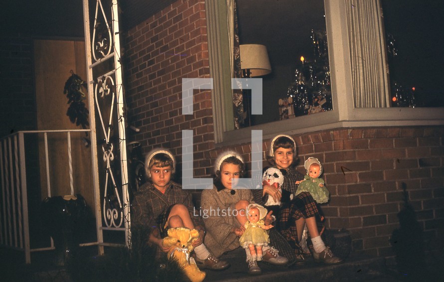 girls sitting on front steps holding dolls 
