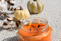 flames on an orange candle, pumpkins, and cotton sprays on a knit blanket 
