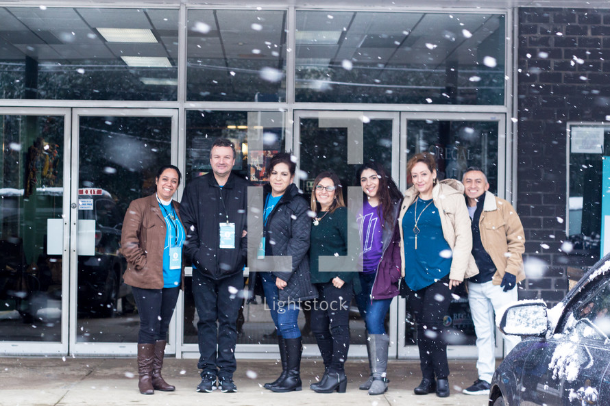 a group of men and women standing together outdoors in falling snow 