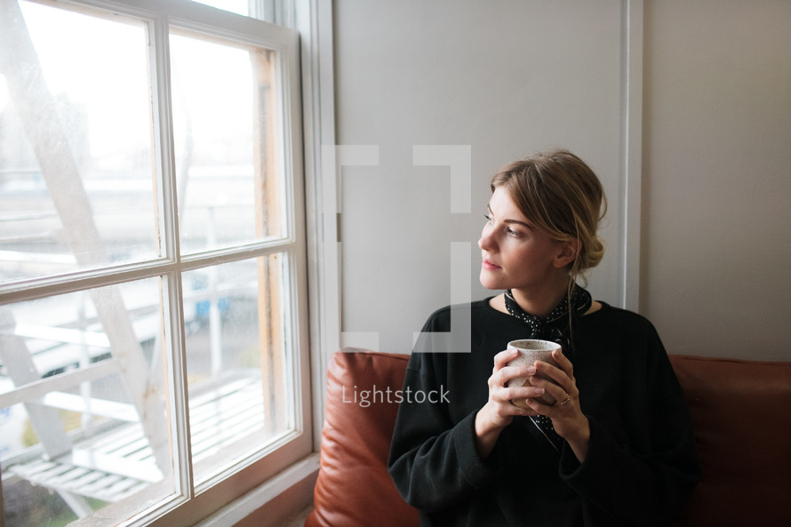 a woman sitting in a window holding a coffee mug
