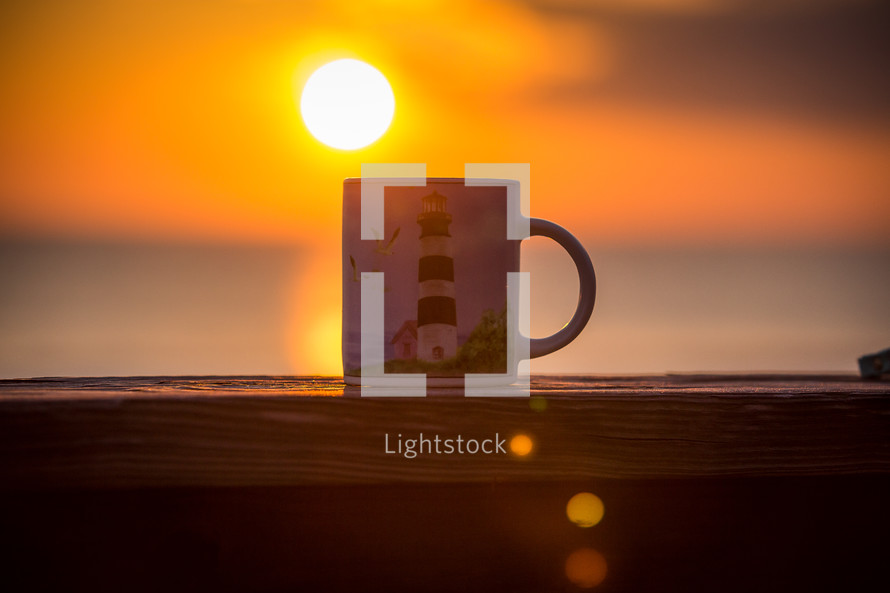 coffee mug with a lighthouse on a banister, and sun a sunrise 