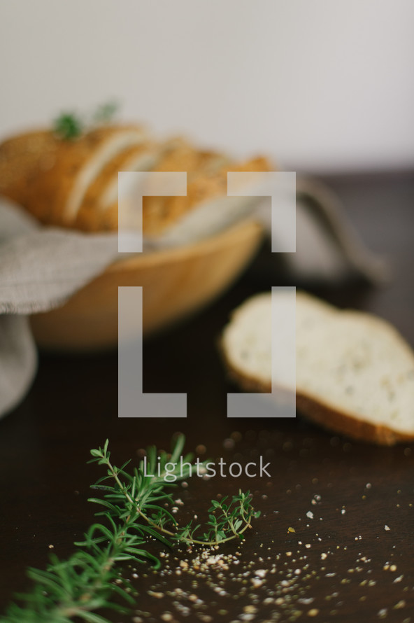 A wooden bowl full of sliced bread and a sprig of rosemary.
