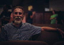 A bearded man sitting in a church auditorium.