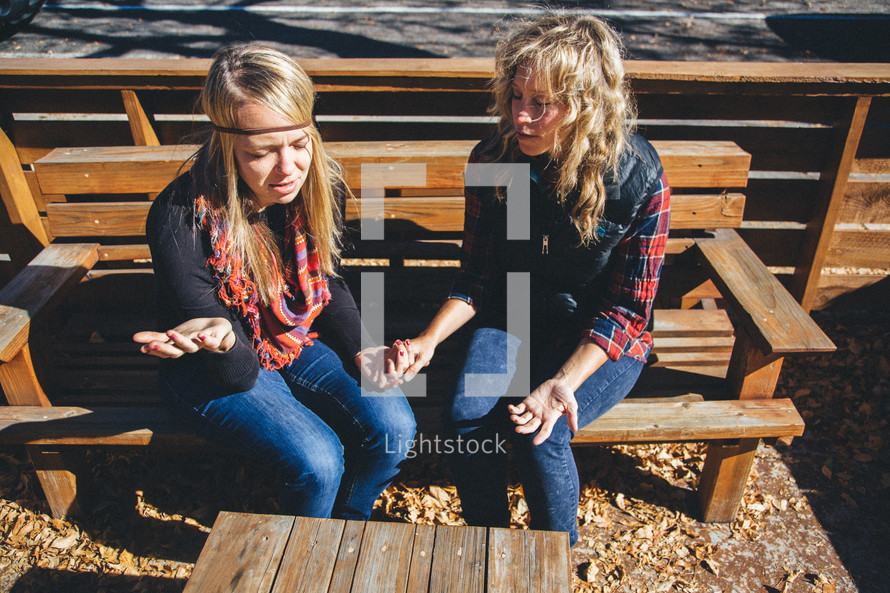 friends sitting on a bench holding hands in prayer 