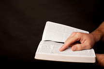 a man with his finger on scripture on the pages of a Bible 