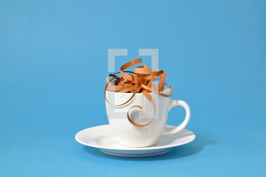 Brown paper spirals in white mug to look like coffee on blue background