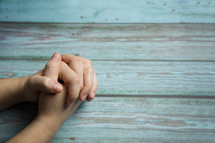 praying hands against a teal wood background 