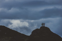 silhouettes of people standing on a peak 
