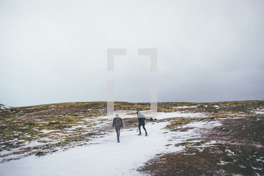 two men hiking up a hill in snow 