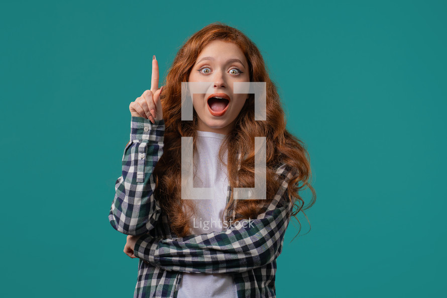 Happy stylish woman having idea eureka moment, pointing finger up on blue background. Clever lady showing answer gesture or remembered what she forgot, memory concept. High quality