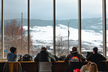 young men sitting at a cafe looking out at a snow covered mountainside 