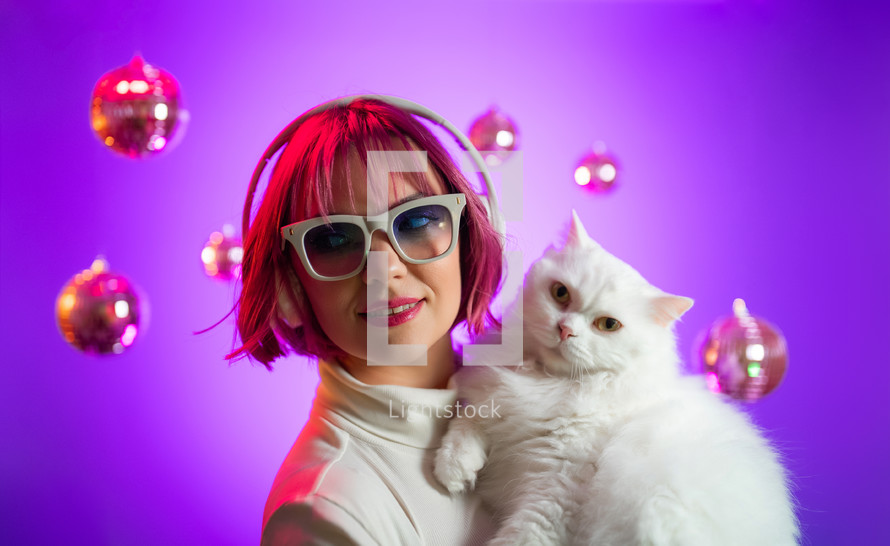 Gorgeous woman with pink dyed hair listening music in headphones. White cat.
