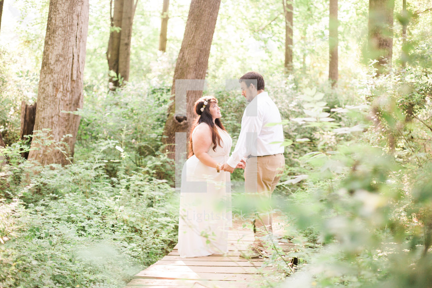 bride and groom holding hands on a wooden path in the woods 
