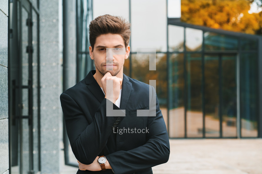 Portrait of young successful confident businessman in the city on office building background. Man in business suit looking to camera and smiling. Portraiture of handsome guy.