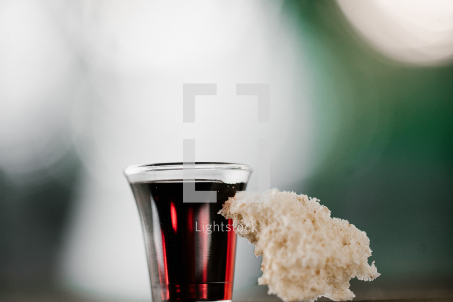 communion wine in a cup and bread against a bokeh background 