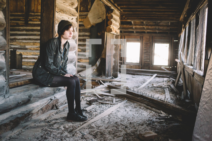 A woman sitting in an unfinished log house.