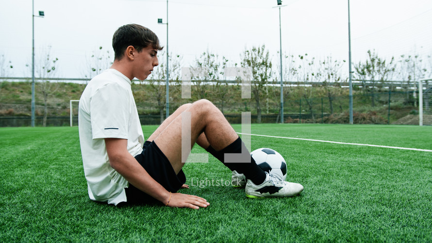 Teenage Soccer Player Sitting on the Side of the Field Breathing Tired