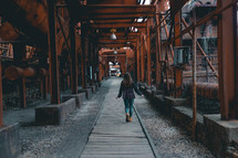 a woman walking under rusty steel beams 
