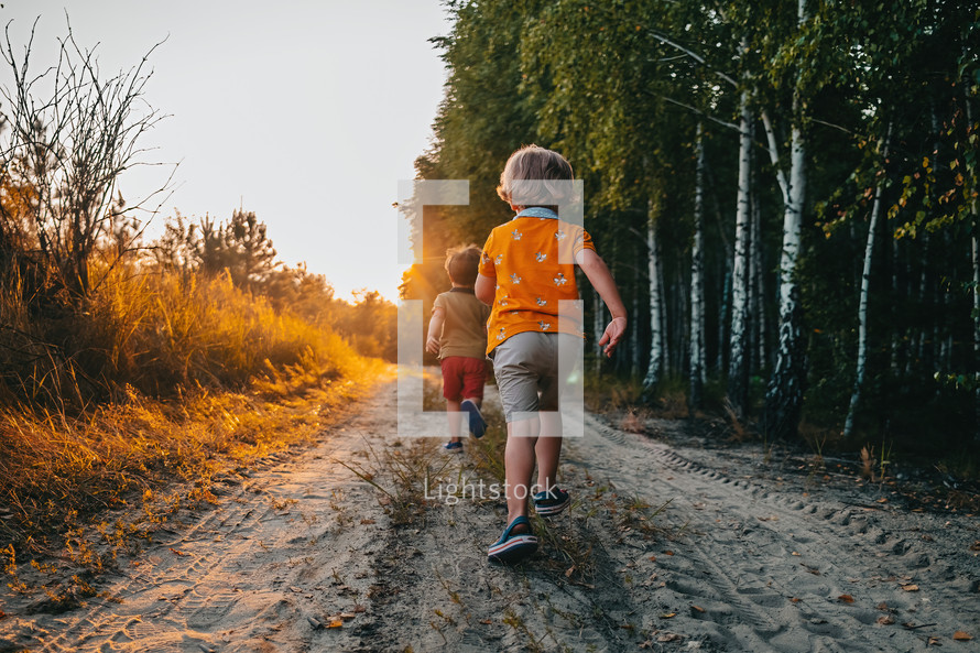 Cute kids, boys runs at summer nature road. Brothers, playing outdoors. Sunset. Happy childhood. High quality photo