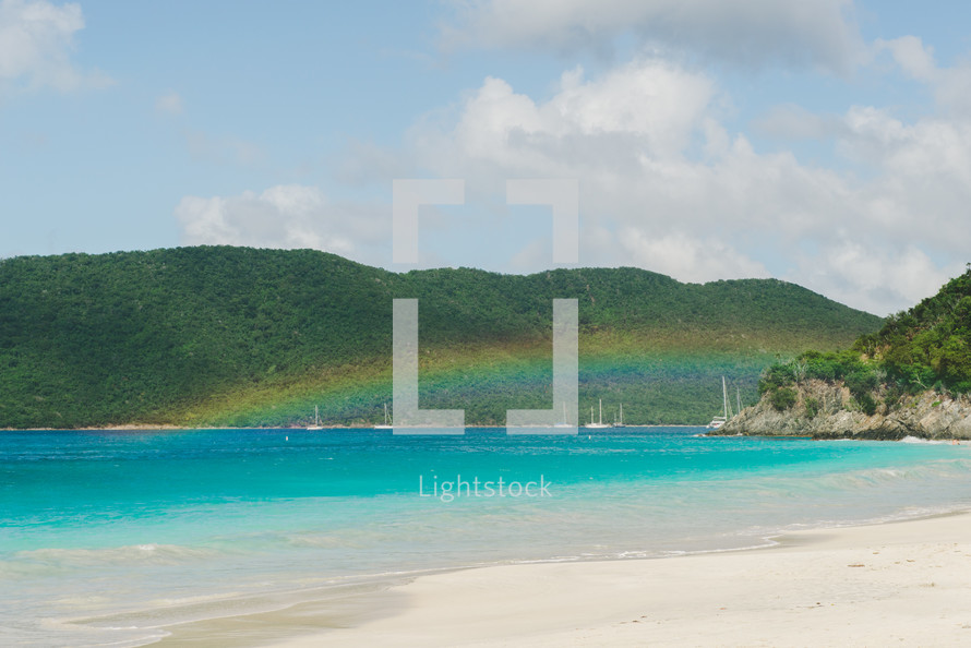 rainbow over sailboats along a beach shore 