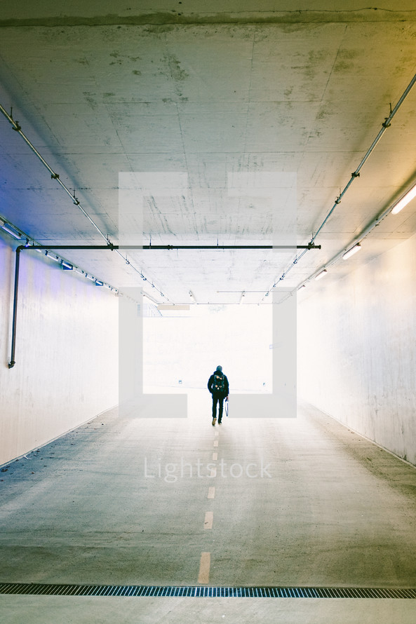 a man walking through a tunnel of a parking garage 