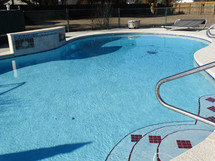 Swimming pool with bright blue water shining in sunlight surrounded by pool deck and waterfall wall