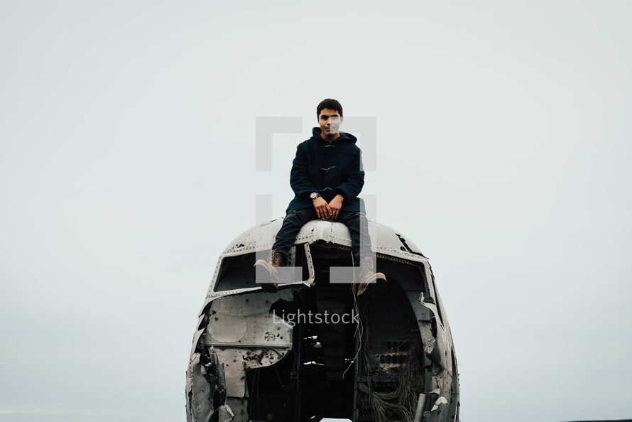 a man sitting on wreckage of an airplane crash site 