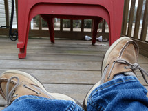 a person's legs laying on porch deck wearing jeans and brown boat shoes with red decor in background