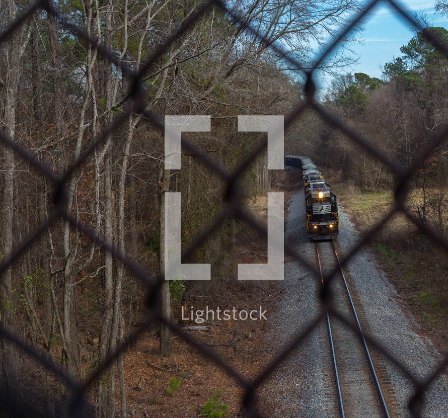 Train on a railroad track as seen through a chain link fence.