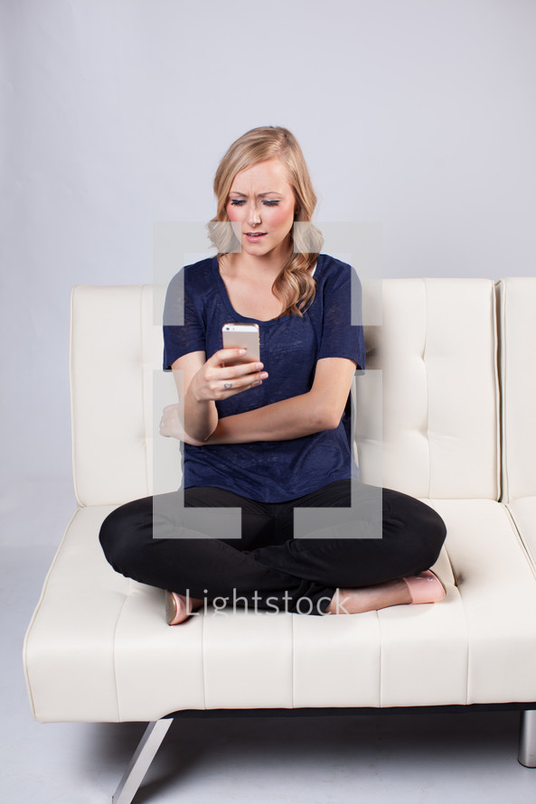 woman texting on a white couch 