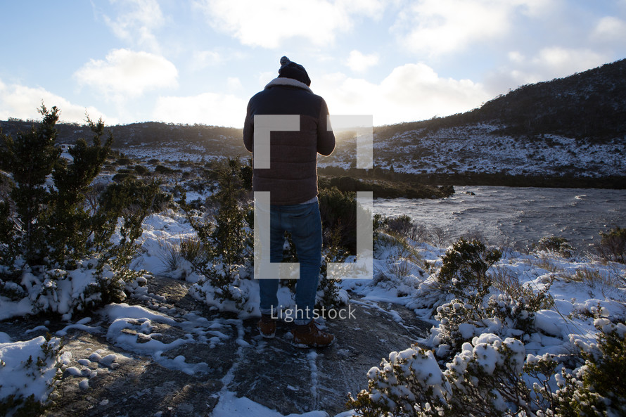 a man standing outdoors in snow by a lake 