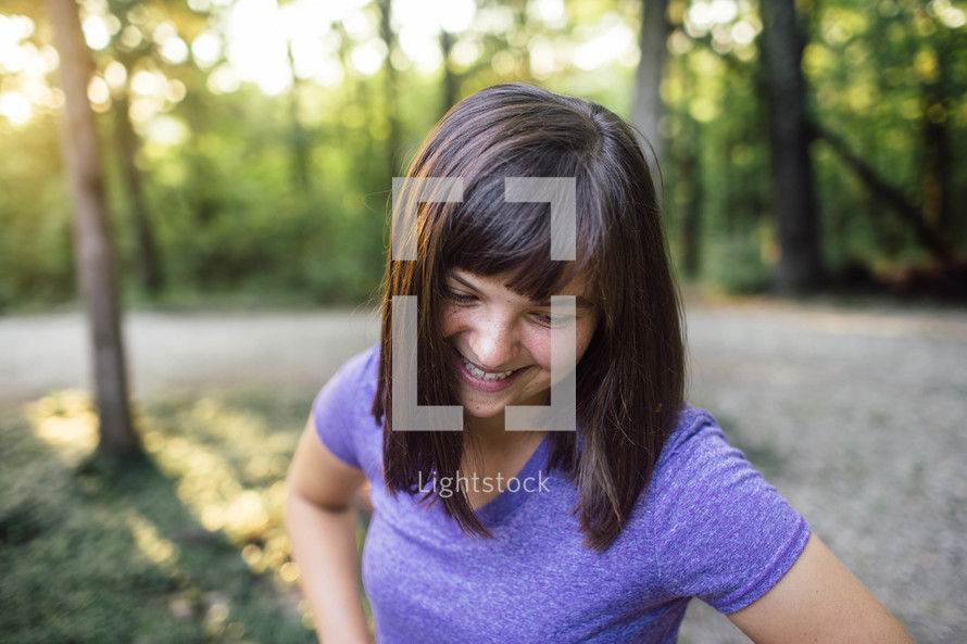 A smiling young woman amid trees.