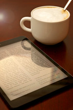 Bible app on a tablet and coffee on a wood table 