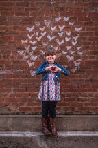 chalk hearts on a brick wall and little girl making a heart shape with her hands 