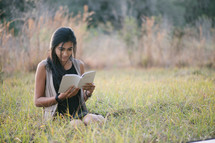 young woman sitting in grass studying scripture 