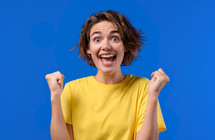 Pretty woman shows triumph yes gesture of victory, she achieved result, goals. Girl glad, happy, surprised excited happy lady on blue background. Jackpot concept. High quality photo
