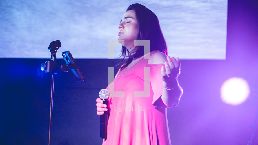 a woman on stage holding a microphone and praying 