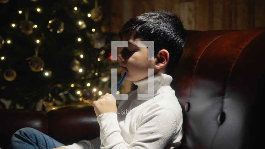 Little Child thinking and writing under Christmas tree 