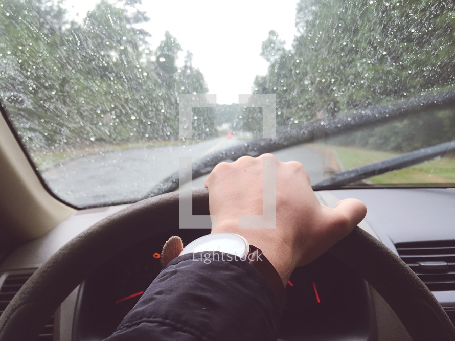 hand on a steering wheel driving in the rain 