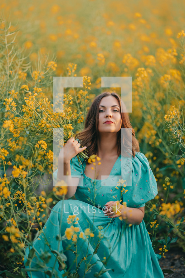 Portrait of attractive woman posing in blooming canola flowers field. Elegant girl in retro dress with straw hat, countryside nature place. Rapeseed meadow, vintage outfit, spring season