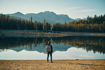 A person standing at the shore of a lake.