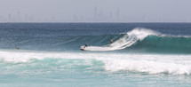 surfer and jet ski in large waves and view of a city 