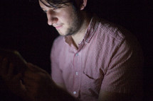 A man illuminated by the light of an electronic tablet.
