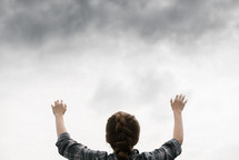 a woman with raised hands standing under a cloudy sky