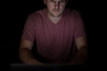 A man illuminated by the light of a computer.