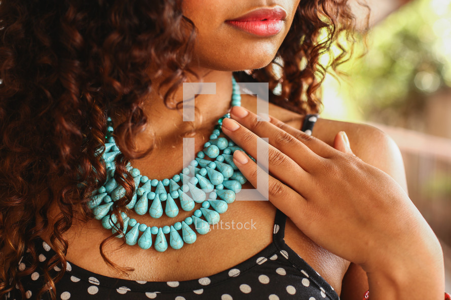 a young woman touching her teal beaded necklace 