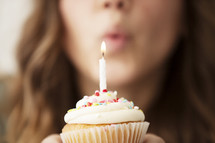 a woman blowing out a candle on a cupcake 
