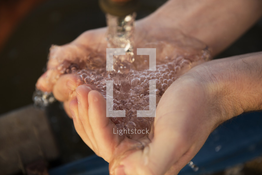 cupped hands holding water from a spigot 